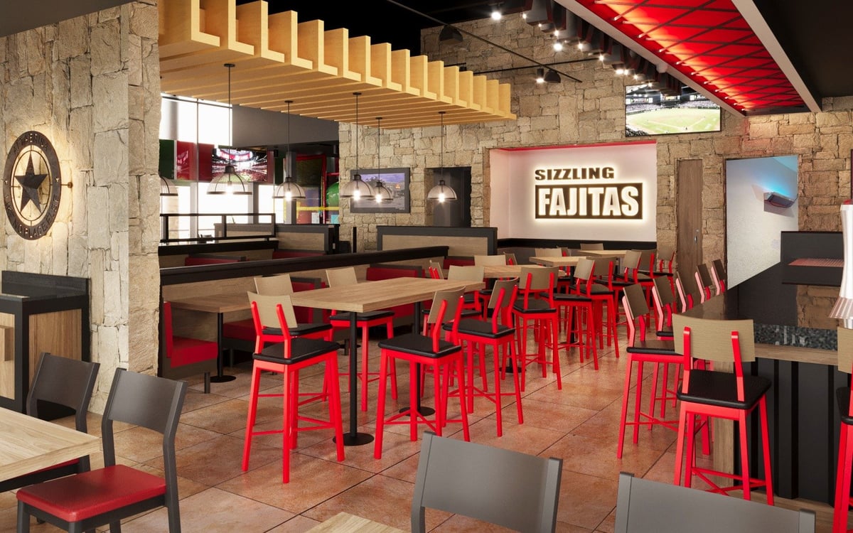 Interior de restaurante con sillas rojas, mesas de madera, paredes de piedra y letrero Sizzling Fajitas